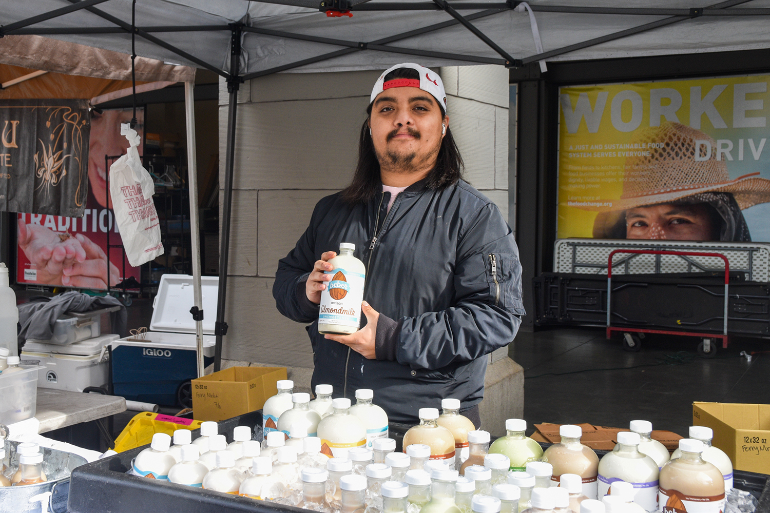 Hecter holds up a bottle of almond milk at Beber Almond Milk's farmers market stand