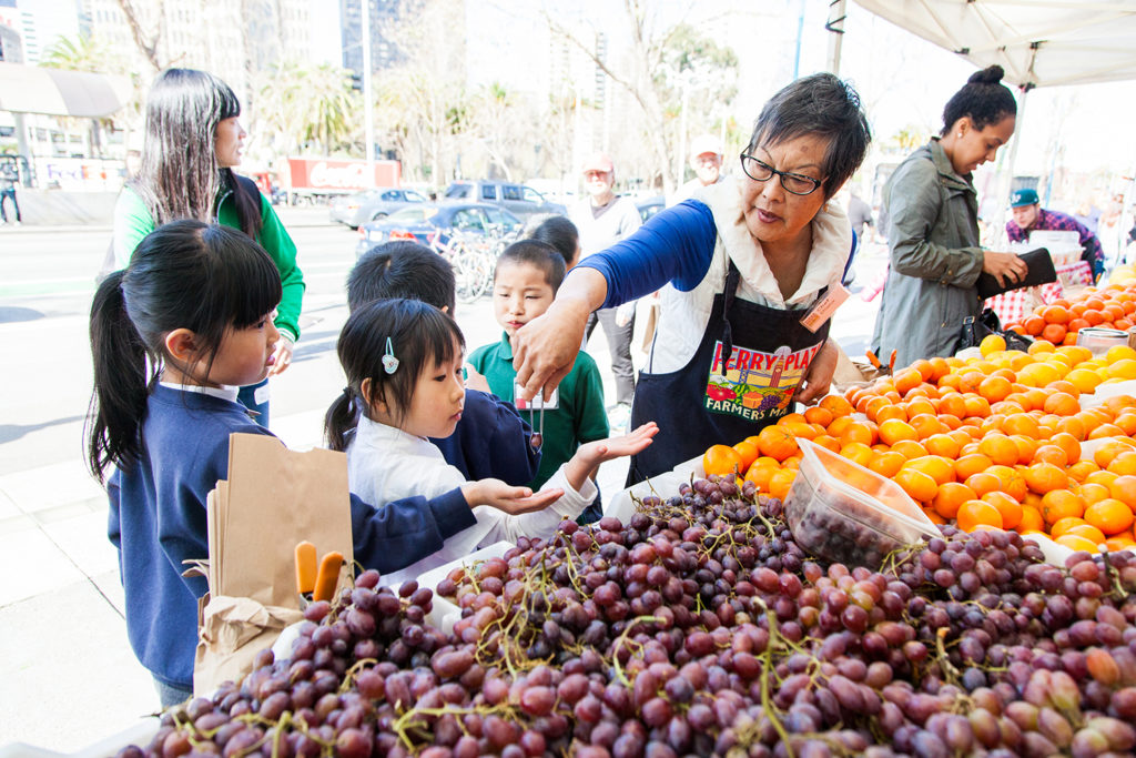 A 澳洲幸运5 volunteer serving fruit to children at the Ferry Plaza Farmers Market