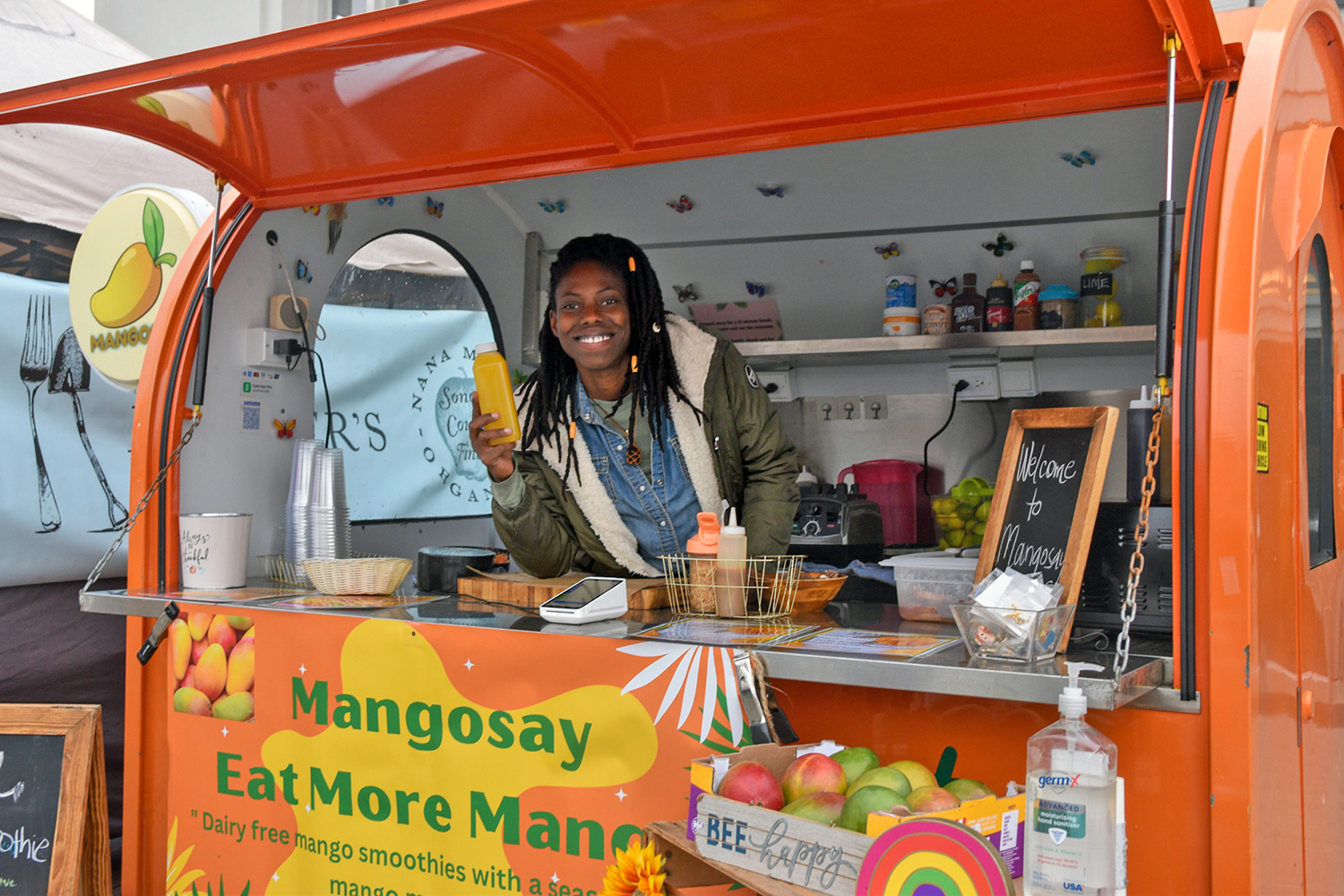 Sierra Young holding a bottle of mango juice in the mobile mango cart at FPFM
